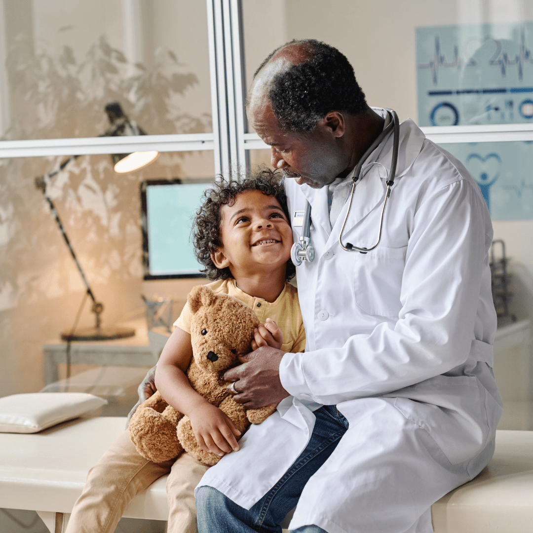 Doctor with a young child on a hospital bed holding a teddy bear, representing pediatric and neonatal cardiac care.